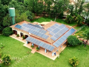 Vista aérea de uma casa com telhado repleto de painéis solares rodeada por vegetação