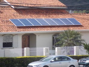 Casa residencial com telhado de telhas com painéis solares, cerca branca e veículo estacionado na frente