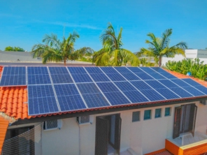 Painéis solares instalados no telhado de uma construção com árvores tropicais ao redor