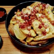 Porção de batata rústica com cheddar e bacon picado.