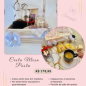 Cesta Mesa Posta da Encantê: baú de madeira aberto com kit americano, caneca com pires, colher de coração, cappuccino, pão de queijo e bolo de cenoura. Cesta de café da manhã artesanal feita à mão em Porto Belo, SC, com entrega em Itapema, Bombinhas e Tijucas. R$ 279,90.