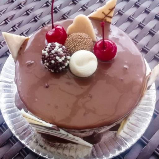 Bolo trufado preto, decorado com cerejas, brigadeiro, bombons e placas de chocolate branco na lateral.