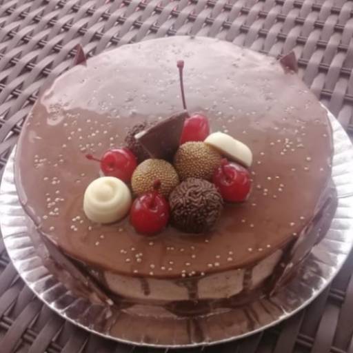 Bolo trufado preto, decorado com cerejas, brigadeiro, bombons  e placas de chocolate preto na lateral.